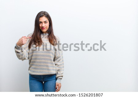 young pretty woman looking proud, confident and happy, smiling and pointing to self or making number one sign isolated against white wall
