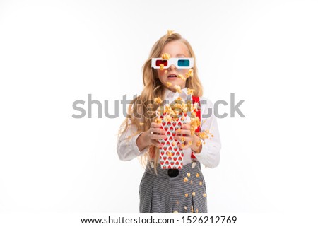 A little girl with long blonde hair in her glasses 3-D eat popcorn.