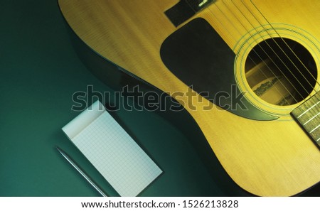 Flat lay an acoustic guitar and a notepad on a green background