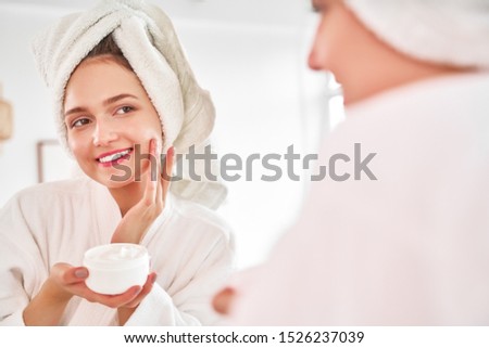 Photo of young woman in bathrobe and with towel on her head reflected in mirror