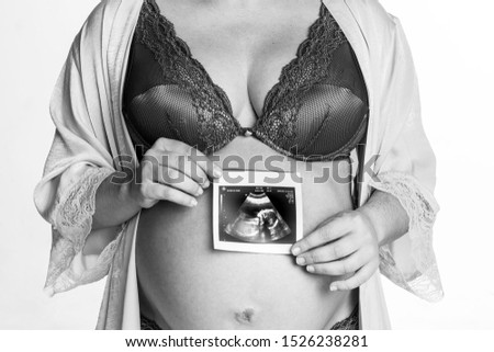 Pregnant women holding ultrasound picture of her future baby on the belly. Motherhood concept. Happy pregnancy, expectation. Black and white picture. White background.
