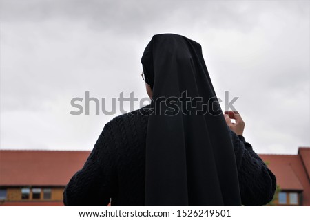 A Nun, Seen From Behind, Looking At The Old Monastery, Germany. Gray Autumn Day Background. Royalty-Free Stock Photo #1526249501