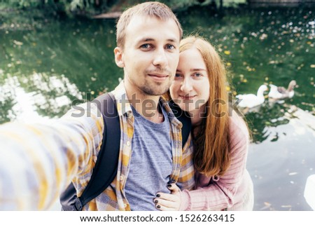 Young married couple makes selfie on the background of a lake with ducks. Cute family content for social networks.