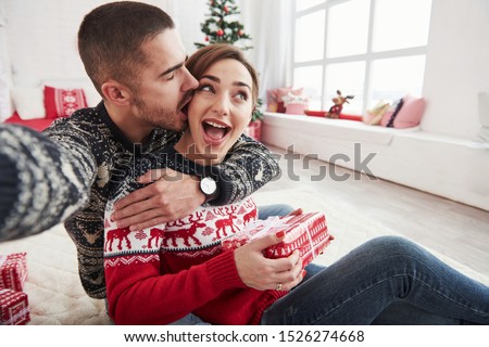 Family picture. Man taking selfie of him and his wife dressed in the Christmas clothes and sitting on the floor of decorative beautiful room.