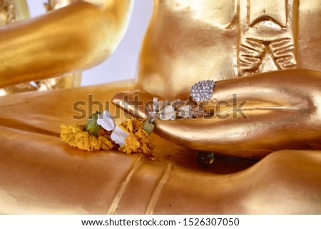 Hand of a golden Buddha statue holding a flower necklace