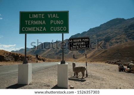 Alpaca on the signs "Limit of the cities of Cusco and Puno" and "The region of Puno wishes a good trip."
