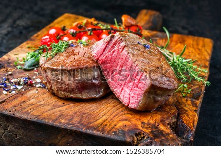 Fried dry aged beef fillet medallion steak natural with tomatoes and herbs as closeup on a wooden cutting board  Royalty-Free Stock Photo #1526385704