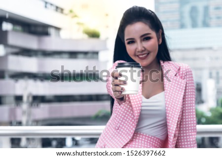 Blurred soft images of Pretty Asian woman Send a cup of coffee with blur building background, to drink concept. This picture focuses on the hand that holds the coffee cup.