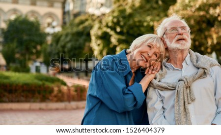 So happy together. Portrait of beautiful senior woman leaning at shoulder of her husband and smiling while standing outdoors on a sunny day