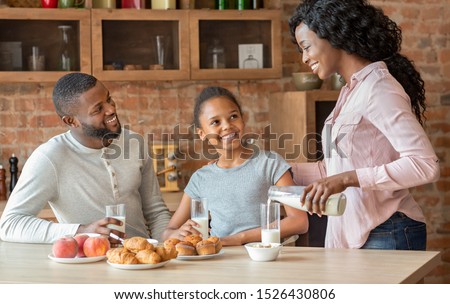 Calcium daily dose. Beautiful black woman pouring milk for her family, copy space Royalty-Free Stock Photo #1526430806
