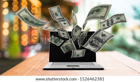Finance and earning concept, one hundred dollar banknotes flying around laptop, internet, side view on dark background.