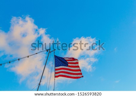 An American ensign blows in the wind as it hangs from a gaff at the stern of a boat.