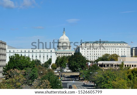 High angle view of the historic Capitol Dome of the United States as it rises above surrounding buildings on the National Mall in Washington, D.C. Green trees line the city street in summer. 