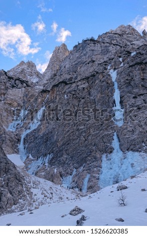 DRONE: Alpinists gather under a frozen river running down the side of a mountain to climb it on a freezing cold winter day. Spectacular shot of a frozen mountain towering above a group of mountaineers