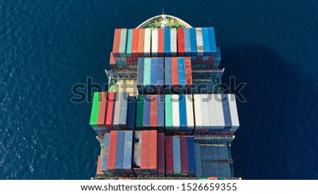 Aerial top down photo of Container cargo Ship carrying load in truck-size colourful containers in deep blue open ocean sea 