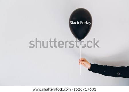 A female hand holds balloon with the inscription Black Friday on a gray wall background