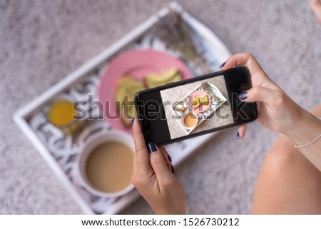 Young woman food blogger takes blog photo of coffee latte, orange juice and avocado fresh toasts. Horizontal photo. detail screen shot mobil phone of healthy breakfast on a tray with mobile phone.