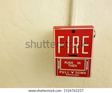 Red emergency fire notifier alarm installed on an ivory wall with word FIRE and instructions on it