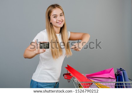 smiling happy woman with credit card and pushcart with colorful shopping bags isolated over grey