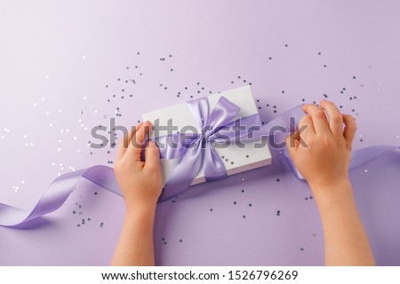 Christmas present stylish gift box in kids hands on lilac background. Creative Flat layout top view composition, mother day, saint valentine, xmas, new year, black friday