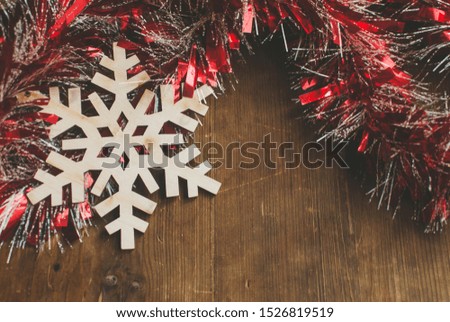 Christmas background with decorative composition of red tinsel and wooden snowflake on wooden board.