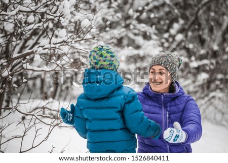 The kid hugs Mom. A boy with his mother on a winter walk. A child in a knitted hat have fun with his mother. The woman plays with her son in the snow. The family spends time together. Family values.