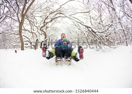 Mother with a child riding on a sled. A woman with her son rides down the hill in a sleigh and screaming. The boy spends time with his parent. Funny winter holidays.
