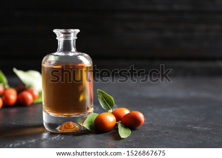 Glass bottle with jojoba oil and seeds on grey stone table against dark background. Space for text