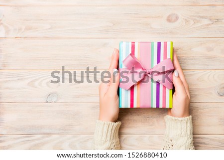 Girl Hands holding craft paper gift box with as a present for Christmas or other holiday on yellow rustic wooden background, top view with copy sppace.
