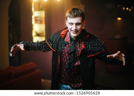 The young man in the Halloween costume of Count Dracula looks ominously at the camera. The guy spread his arms