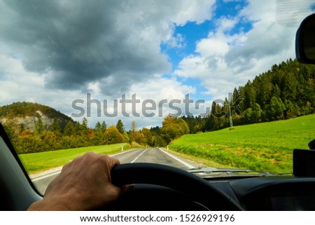 View of the road with a beautiful mountain landscape from the car window in a nice summer or autumn day. Woman's hand on the steering wheel. Female driver and beautiful landscape during travel in auto