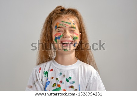 Little girl in white t-shirt, with painted face is making grimaces while posing isolated on white. Art studio. Close-up.