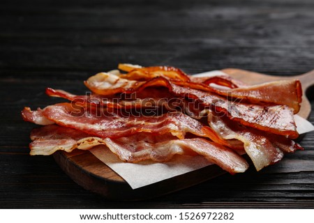 Slices of tasty fried bacon on black wooden table, closeup Royalty-Free Stock Photo #1526972282