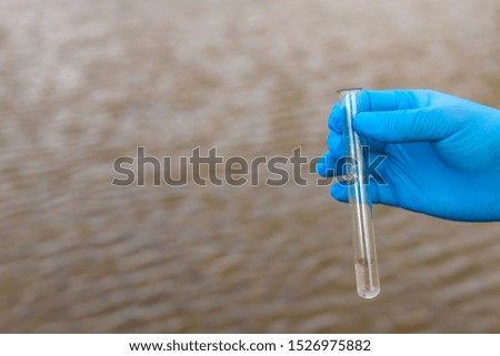 Sample water from the river for analysis. Hand in glove holding a test tube.ecology concept