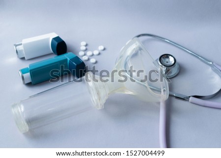 Treatment of asthma and lung conditions. Bronchodilator, anti-inflammatory, mask and inhalation chamber to control asthma due to allergies or colds on a gray background. Royalty-Free Stock Photo #1527004499