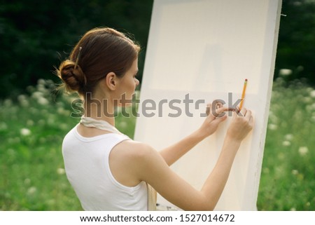 woman in a white dress on a green clearing draws a picture