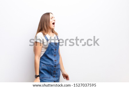 young pretty woman screaming furiously, shouting aggressively, looking stressed and angry against white wall
