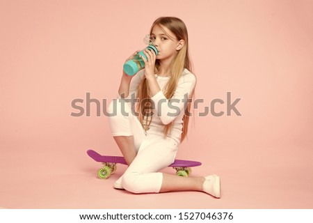 Water gives her energy. Little girl skater drinking water on pink background. Thirsty child drinking fresh water from plastic bottle. Little girl having a drink from water bottle sitting on penny