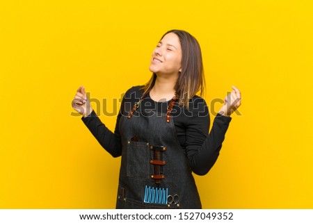 hairdresser woman smiling, feeling carefree, relaxed and happy, dancing and listening to music, having fun at a party against orange background