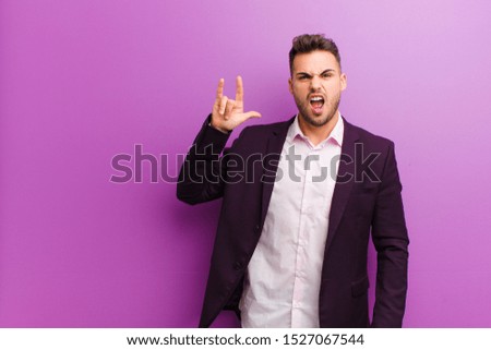 young hispanic man feeling happy, fun, confident, positive and rebellious, making rock or heavy metal sign with hand