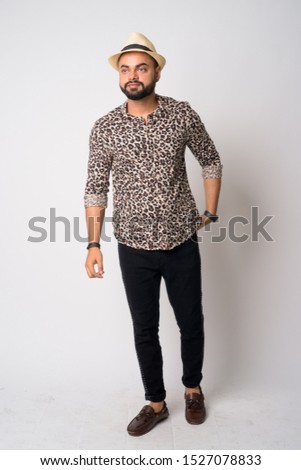 Full body shot of young bearded Indian man with hat thinking