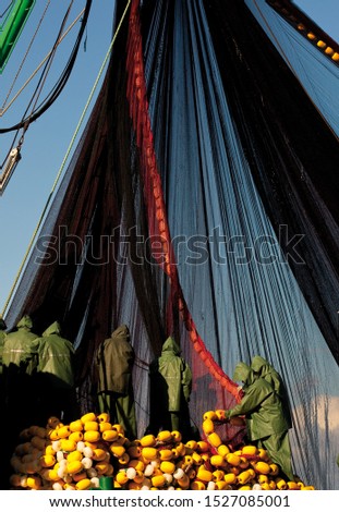 Fishermen, industrial fishing equipment and nets. Natural light, blue sky in the background. Vertical close-up shot.