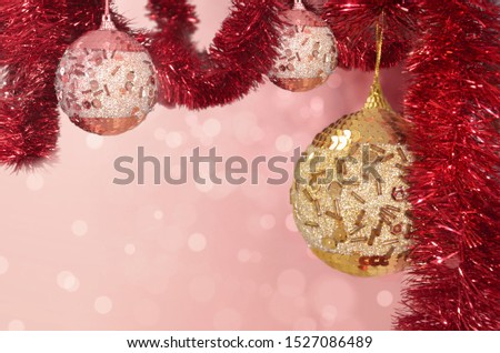 Beautiful Christmas balls on a garland of red tinsel on a blurry background with bokeh in pink, red and gold colors