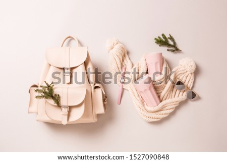 Winter fashion accessories or christmas gifts. White leather backpack, woollen scarf, pastel pink  mugs, watch and sunglasses. Captured from above (top view, flat lay) on grey background.