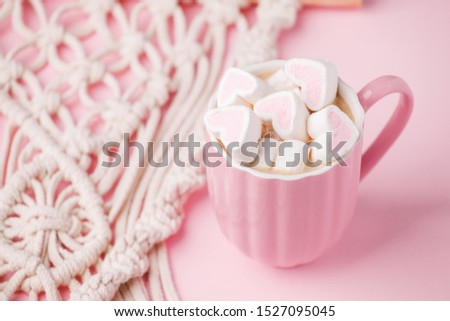Cup of hot chocolate with pink heart shaped marshmallows and macrame panel on pink background, trendy minimal romantic composition, saint valentine morning, banner