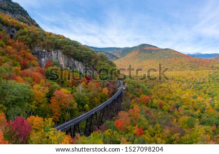 Brightly colored fall foliage during a sunny fall day. Aerial drone shot red, yellow and orange fall leaves with train tracks curving around mountain. Royalty-Free Stock Photo #1527098204