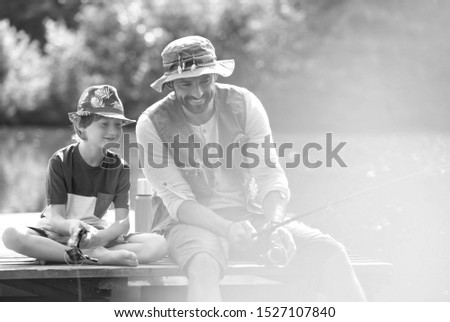 Black and white photo of father and son catching fish in pier at lakeshore