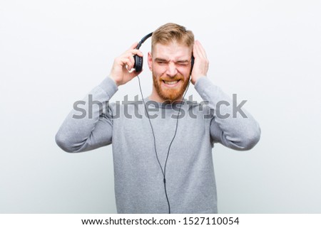 young red head man listening music with headphones against white background
