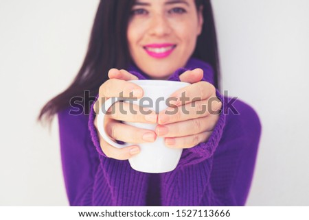 Close up of a beautiful young woman holding a cup of hot coffee in winter outfit at home