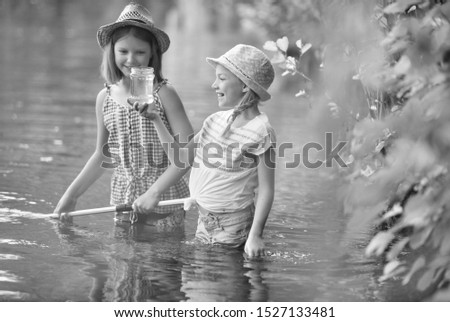 Black and white photo of Smiling young girl showing jar to a friend while standing in lake